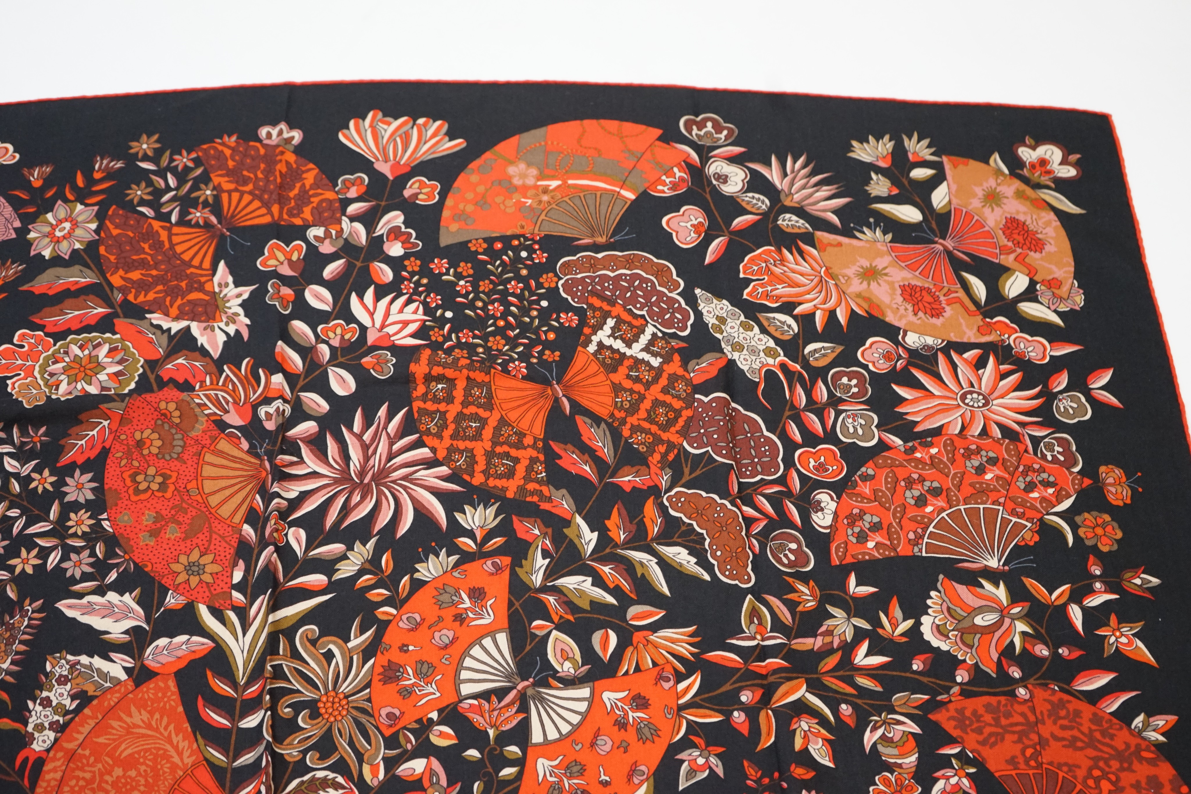 An Hermes wool scarf, with fan and flower motifs on a black ground, in Hermes cloth bag 132 cm.